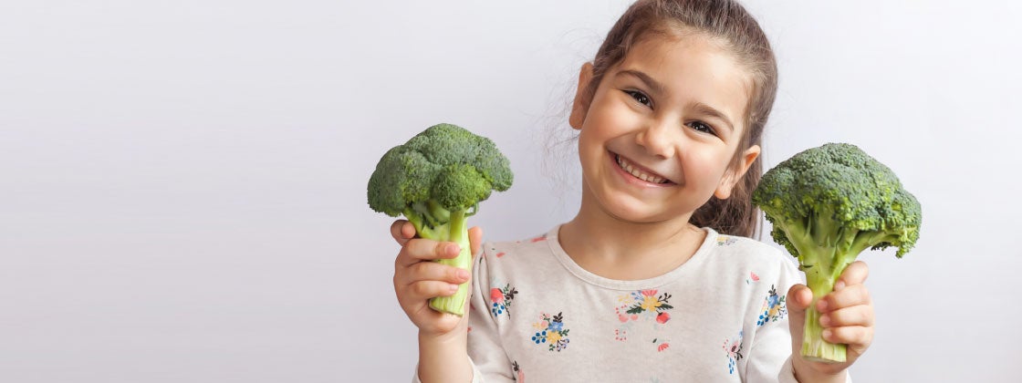 niña sonriendo con brócolis en manos