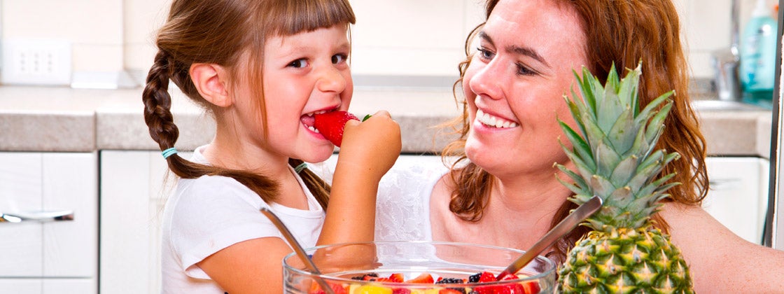 Mamá le da a su hija una ensalada de frutas en la cocina
