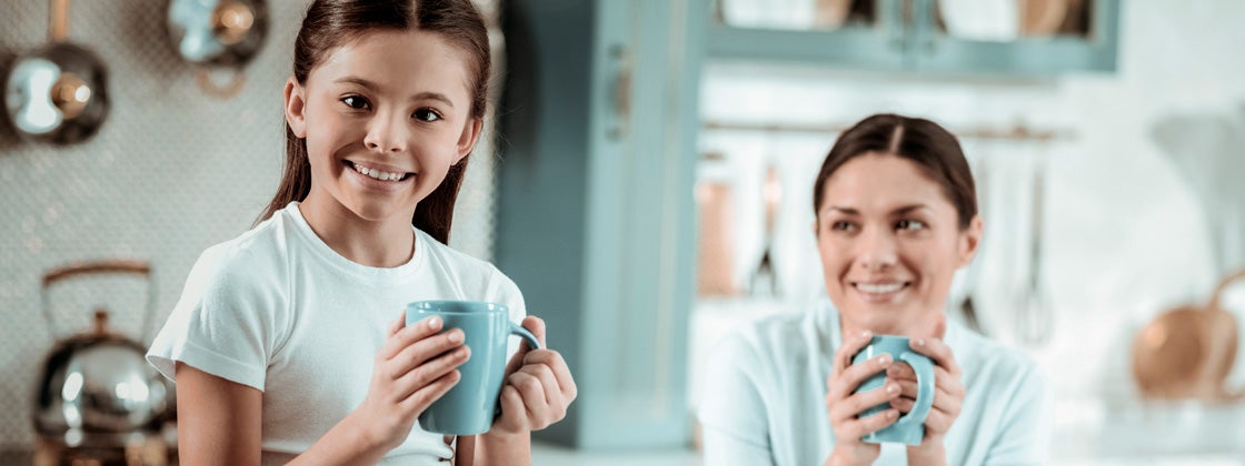 Una niña sostiene una taza en el mesón de la cocina con su madre en el desayuno