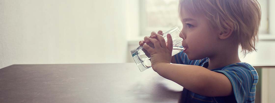 Niño bebe un vaso de agua en la cocina porque es importante para la salud